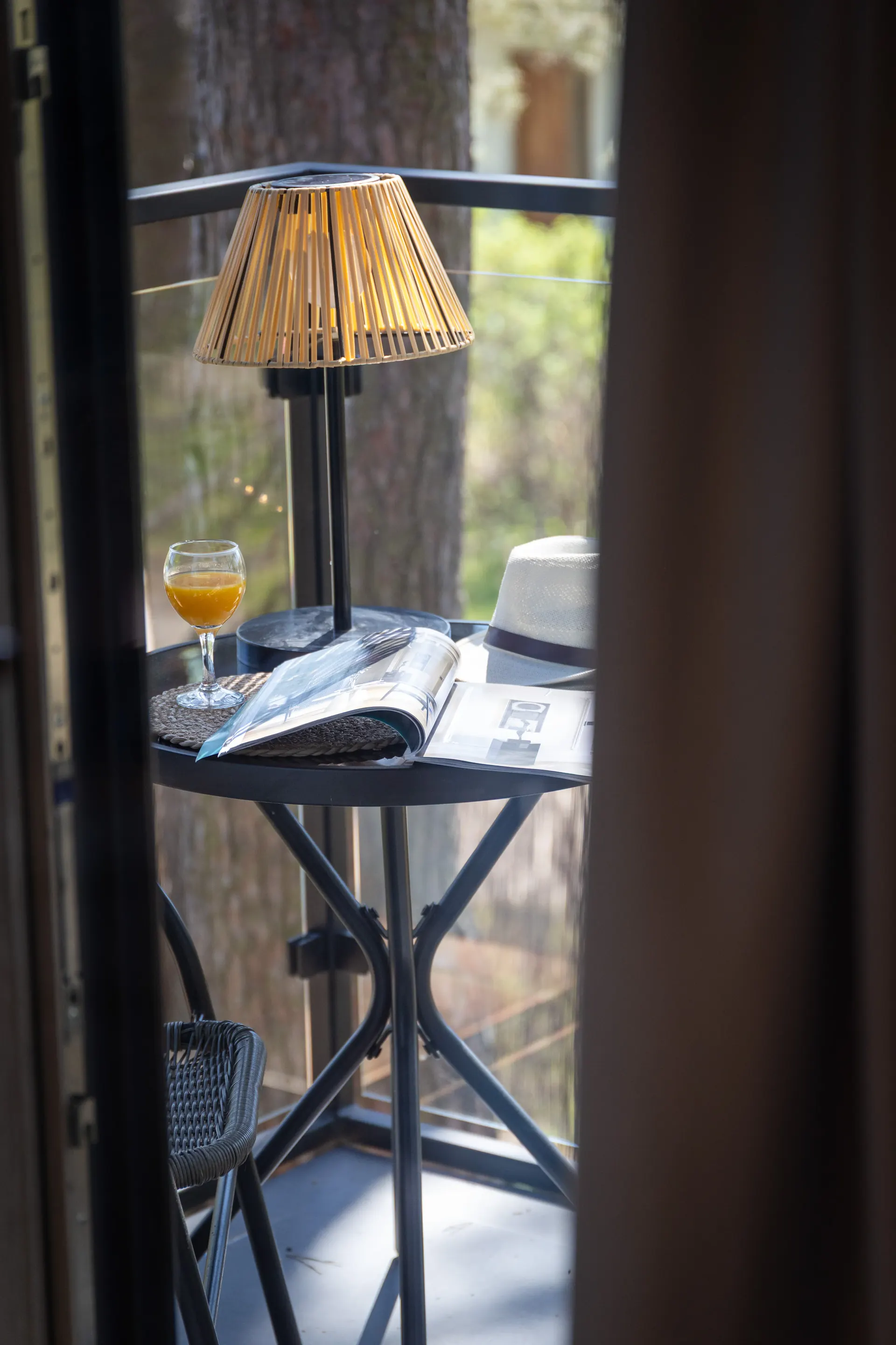 Taras z okrągłym stolikiem bistro, lampą i sokiem pomarańczowym, widok na las sosnowy — Apartament 1 Poezja Ciszy Dębki